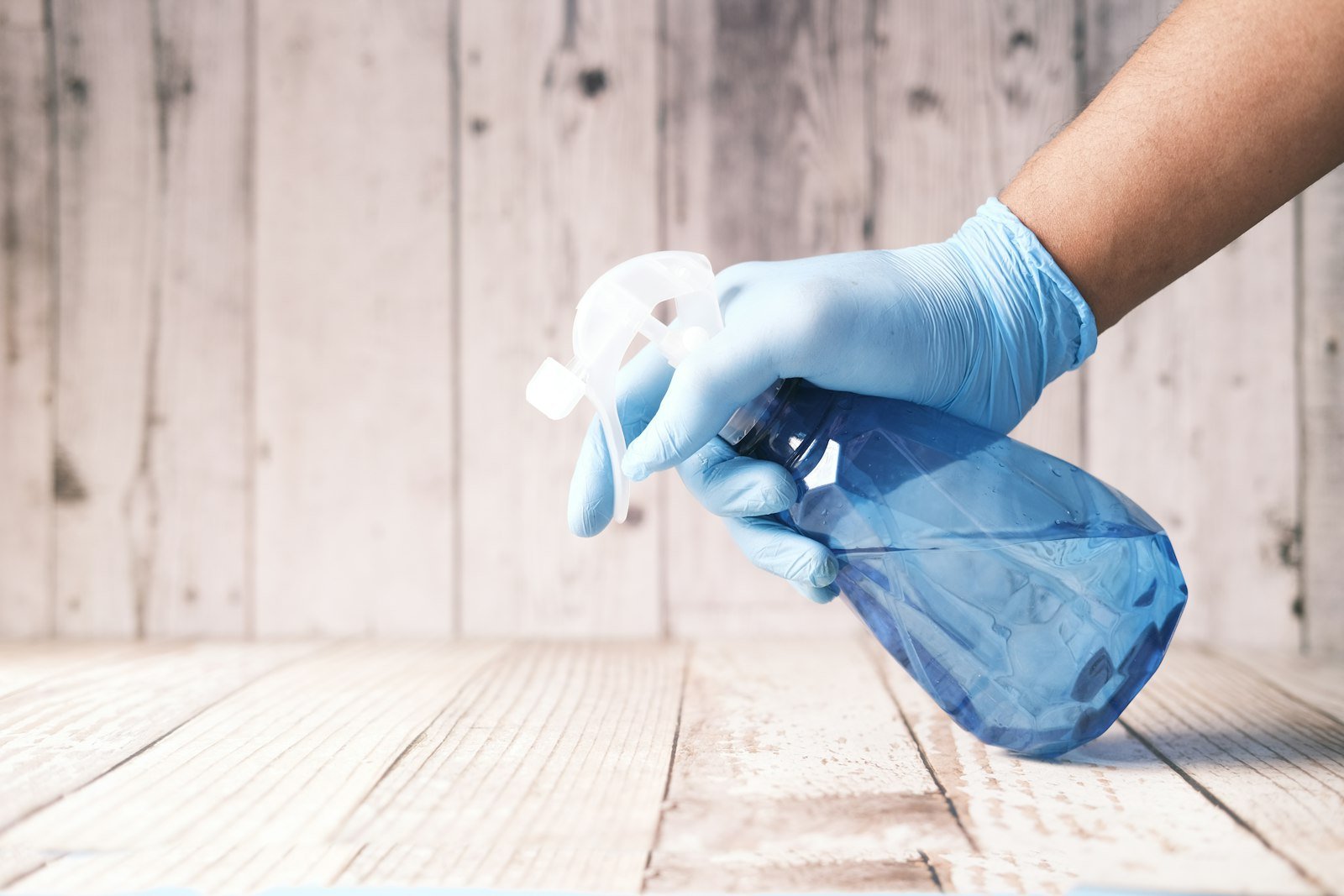 Hand in blue gloves holding a spray bottle, preparing for commercial cleaning on wooden surface, emphasizing professional cleaning services in Devizes.