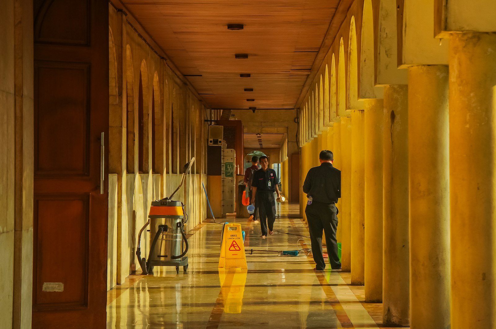 Communal area cleaning in progress, featuring workers maintaining a corridor with polished floors, cleaning equipment, and a caution sign, emphasizing Chippenham Cleaning's service focus on shared spaces.