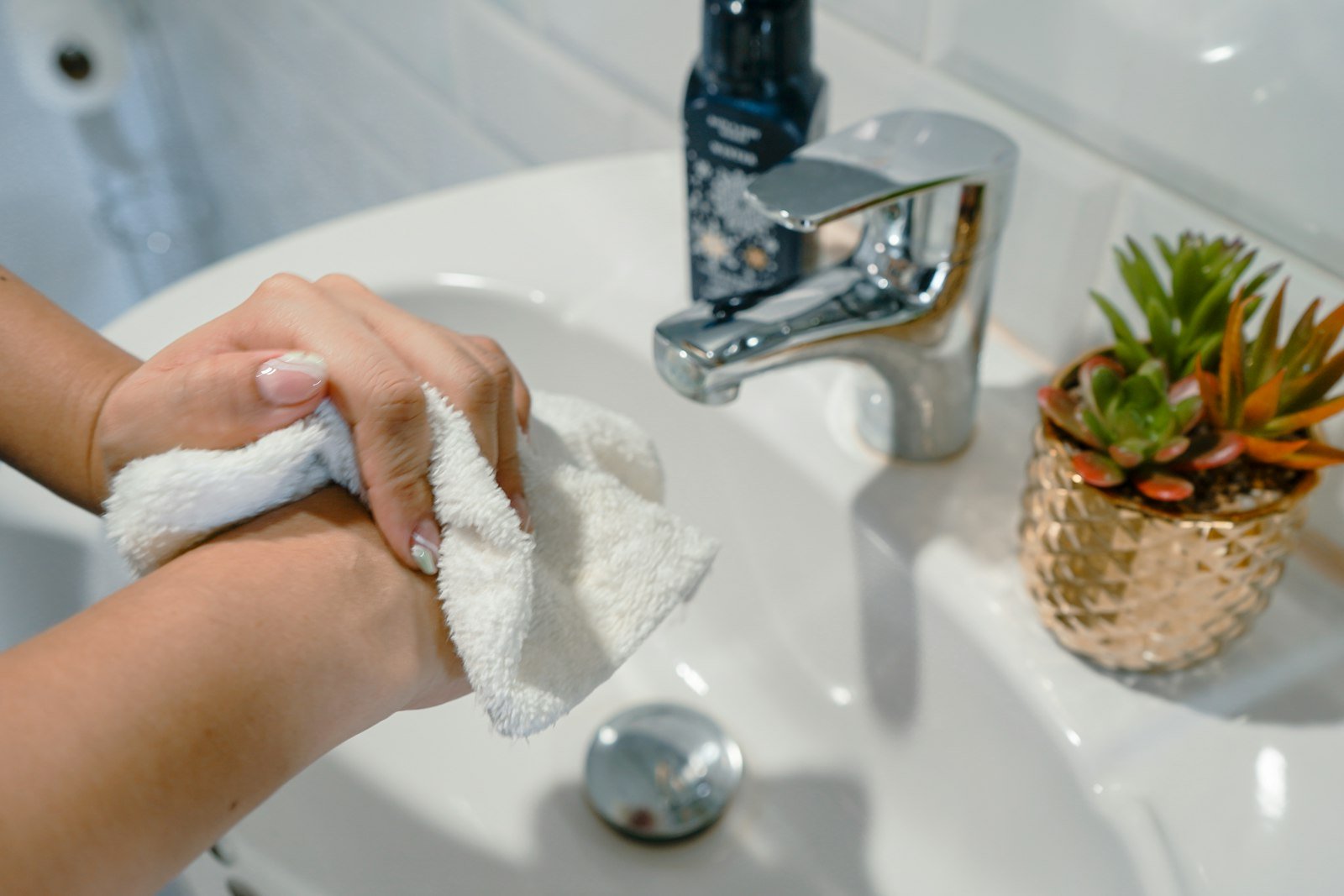 Person cleaning hands with a white towel at a sink, featuring a chrome faucet and a decorative plant, illustrating deep cleaning practices relevant to Chippenham Cleaning services.