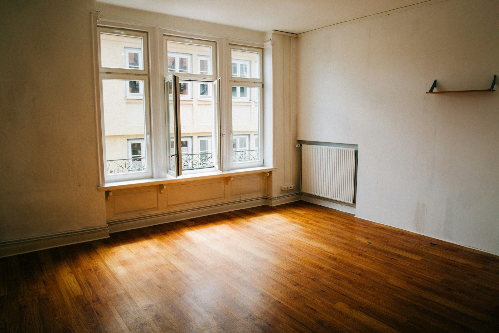 Bright, empty room with large windows, wooden flooring, and a radiator, representing end of tenancy cleaning service by Chippenham Cleaning.
