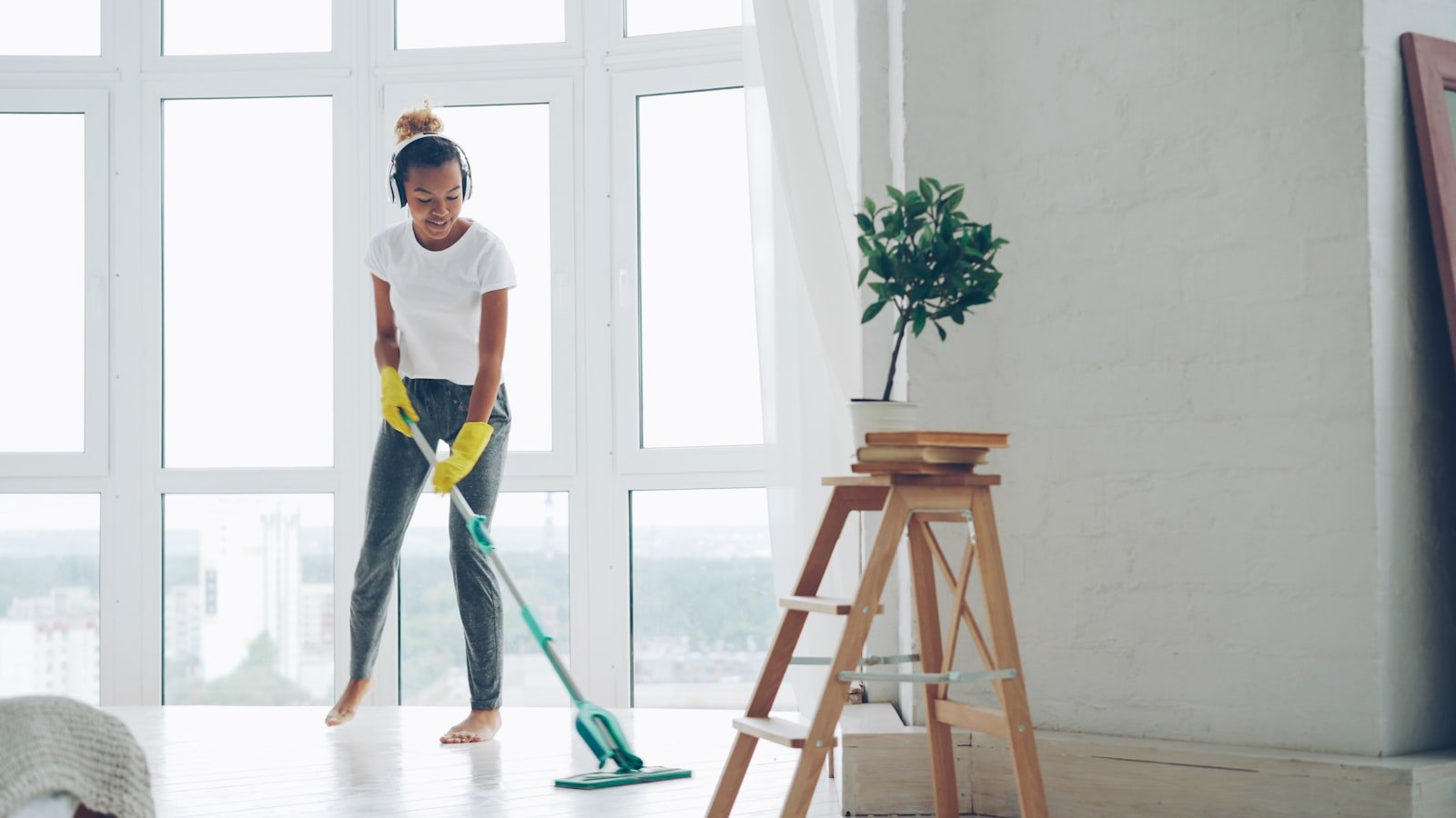 Woman in yellow gloves cleaning office floor with mop, bright windows in background, representing professional office cleaning services in Calne.